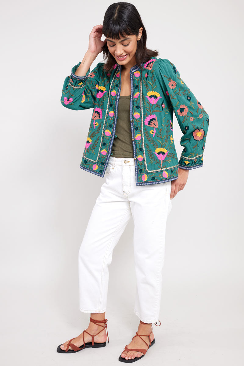 Model tucking hair back and looking down wearing East Eve Emerald Embroidered Jacket