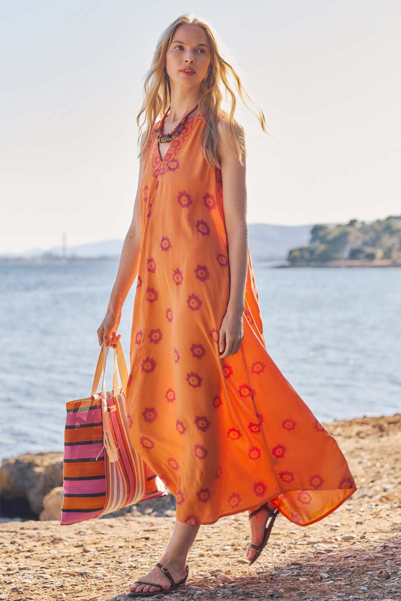 Model walks near the beach wearing East Nevaeh Sleeveless dress and carries Recycled HDPE Pink and Orange Stripe Market Bag